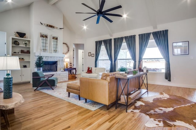 living room with beam ceiling, high vaulted ceiling, light hardwood / wood-style flooring, ceiling fan, and a fireplace