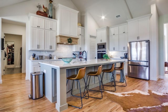 kitchen with appliances with stainless steel finishes, a center island with sink, and white cabinets