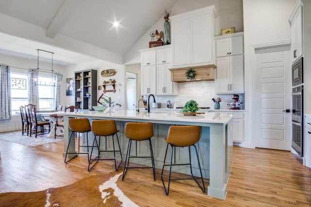 kitchen with appliances with stainless steel finishes, white cabinets, a kitchen bar, hanging light fixtures, and a center island with sink