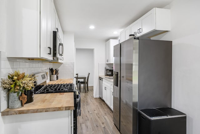 kitchen featuring appliances with stainless steel finishes, tasteful backsplash, white cabinetry, wooden counters, and light wood-type flooring