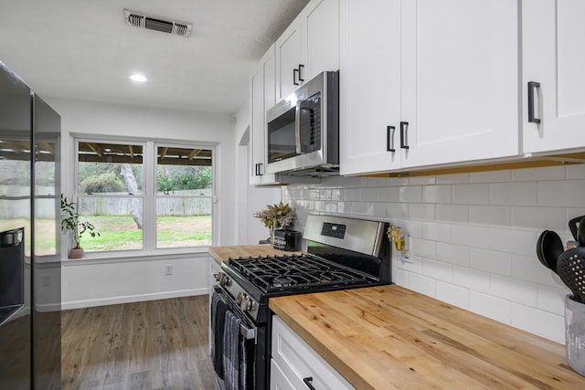 kitchen with appliances with stainless steel finishes, butcher block counters, wood-type flooring, white cabinets, and decorative backsplash