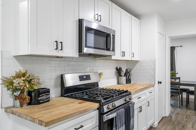 kitchen featuring appliances with stainless steel finishes, wood counters, white cabinets, backsplash, and light hardwood / wood-style floors