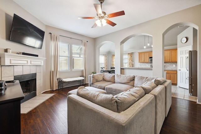 living room featuring a tiled fireplace, dark hardwood / wood-style floors, and ceiling fan