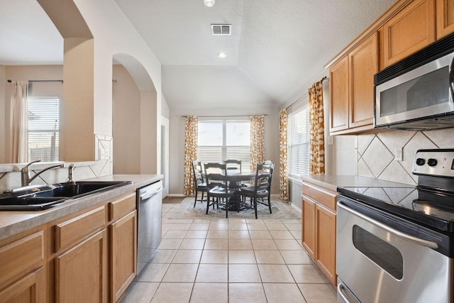 kitchen featuring lofted ceiling, sink, light tile patterned floors, appliances with stainless steel finishes, and backsplash