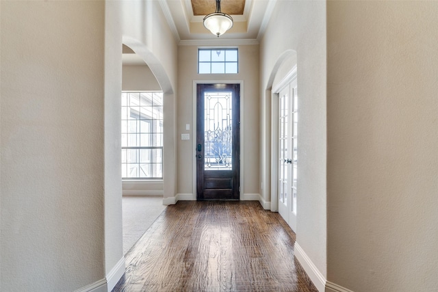 foyer entrance with arched walkways, a raised ceiling, ornamental molding, wood finished floors, and baseboards