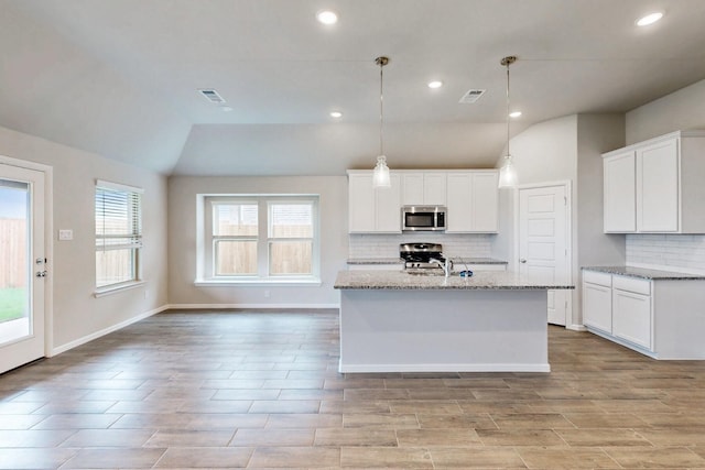 721 Merry Summit Rd, Lavon, TX 75166 - kitchen featuring appliances with stainless steel finishes, lofted ceiling, decorative backsplash, light stone countertops, and a kitchen island with sink
