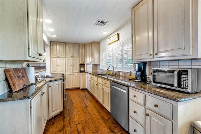 kitchen featuring sink, decorative backsplash, stainless steel appliances, and dark stone counters