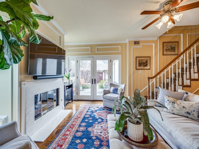 living room featuring light hardwood / wood-style flooring, ceiling fan, a fireplace, ornamental molding, and french doors