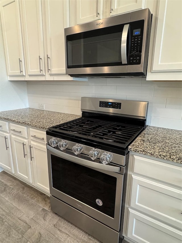 kitchen featuring white cabinetry, backsplash, light stone countertops, and stainless steel appliances