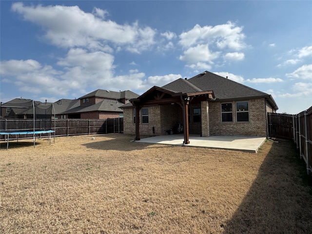 rear view of property with a trampoline, a patio, and a yard