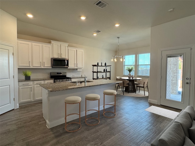 kitchen with a center island with sink, sink, light stone counters, white cabinetry, and stainless steel appliances