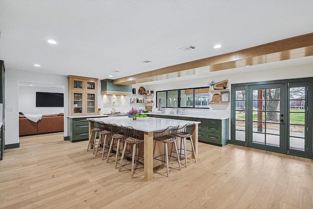 kitchen with sink, a breakfast bar area, green cabinetry, light hardwood / wood-style flooring, and a kitchen island