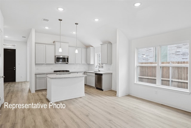 kitchen featuring appliances with stainless steel finishes, pendant lighting, tasteful backsplash, a center island, and light hardwood / wood-style floors