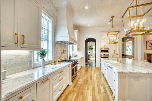 kitchen featuring tasteful backsplash, arched walkways, light stone countertops, custom exhaust hood, and stainless steel appliances