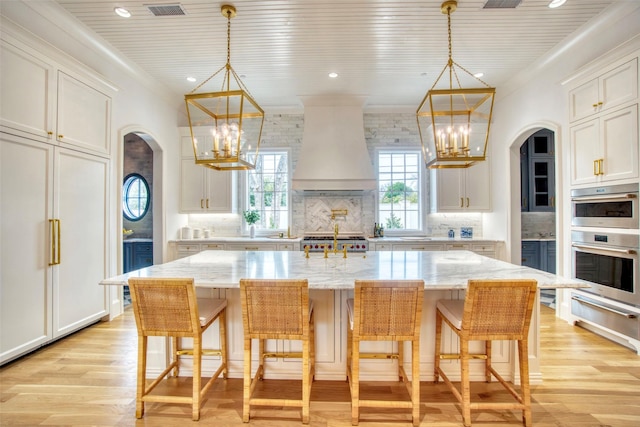 kitchen with a chandelier, stainless steel double oven, custom range hood, and a warming drawer