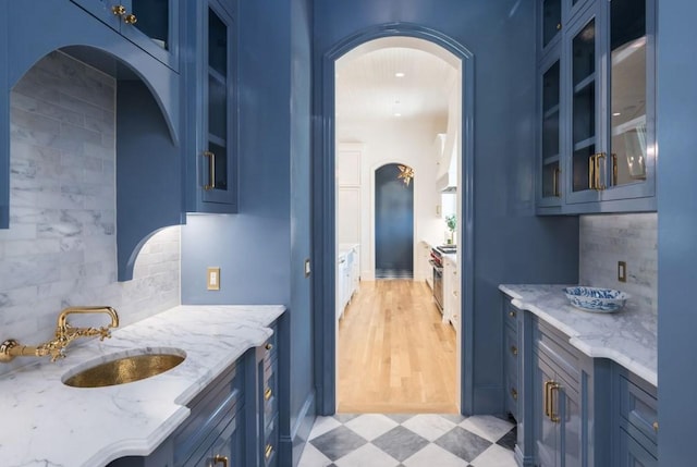 kitchen with blue cabinets, light stone countertops, glass insert cabinets, and a sink