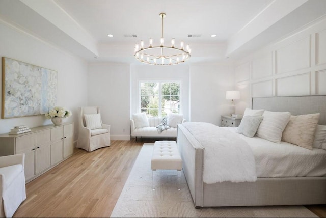 bedroom with visible vents, a tray ceiling, light wood-type flooring, a decorative wall, and a notable chandelier