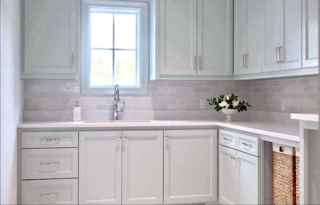 kitchen featuring light countertops, a sink, backsplash, and white cabinetry