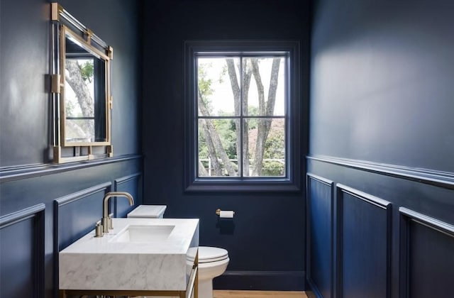 half bath featuring wood finished floors, a sink, toilet, and baseboards