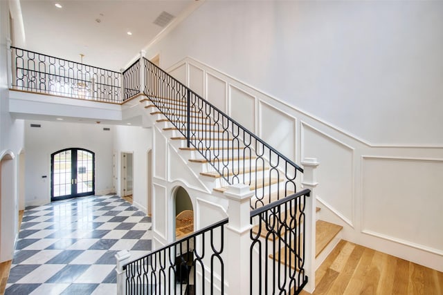 stairway with arched walkways, a decorative wall, a high ceiling, visible vents, and french doors