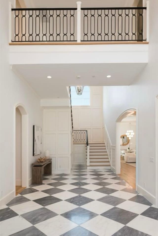 hall with arched walkways, a towering ceiling, baseboards, tile patterned floors, and an inviting chandelier