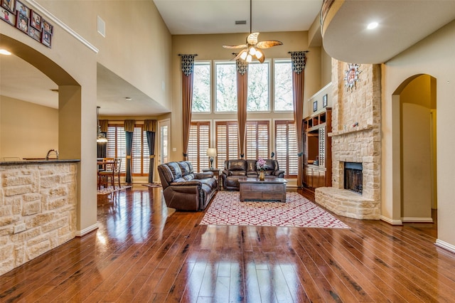 living room with wood-type flooring, a towering ceiling, ceiling fan, and a fireplace