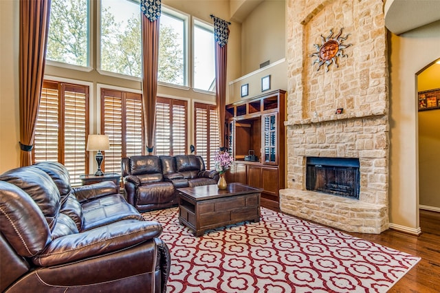 living room with hardwood / wood-style flooring, a stone fireplace, and a high ceiling