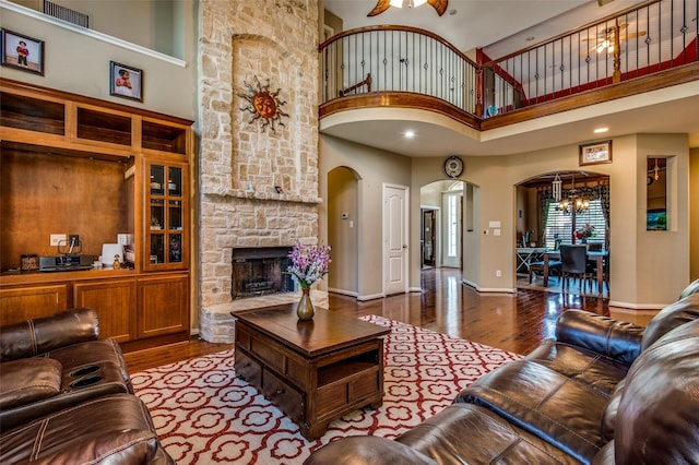 living room with a high ceiling, ceiling fan with notable chandelier, a stone fireplace, and hardwood / wood-style floors