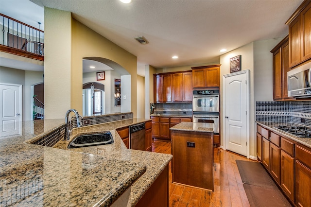 kitchen featuring appliances with stainless steel finishes, sink, a center island, kitchen peninsula, and light stone countertops