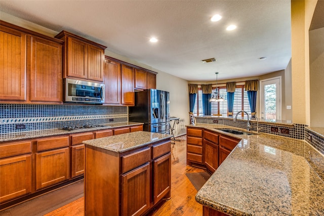 kitchen featuring sink, light stone counters, a center island, appliances with stainless steel finishes, and pendant lighting