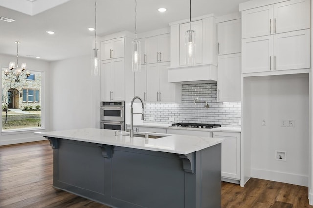 kitchen with decorative light fixtures, a sink, a kitchen island with sink, and white cabinets