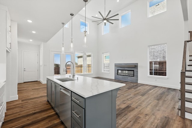 kitchen featuring light stone counters, a sink, hanging light fixtures, stainless steel dishwasher, and gray cabinets