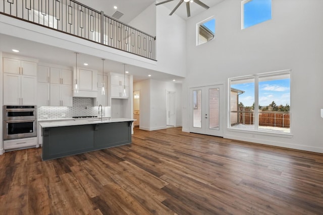 kitchen featuring a center island with sink, white cabinetry, light countertops, and stainless steel double oven