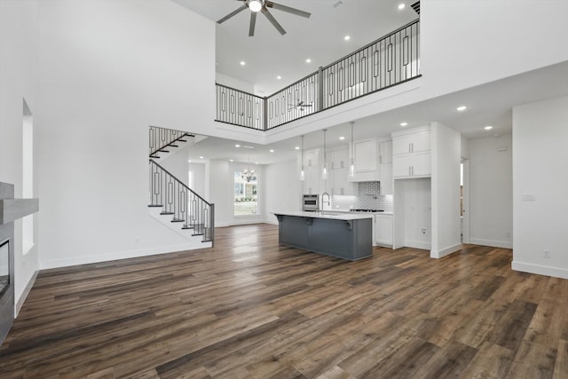 unfurnished living room featuring dark wood-style floors, ceiling fan with notable chandelier, baseboards, and stairs