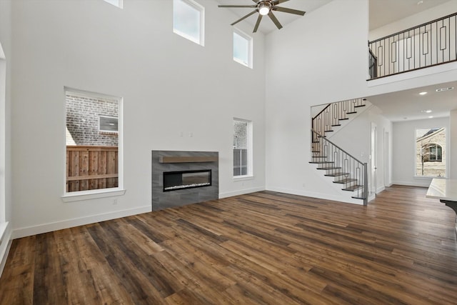 unfurnished living room with stairs, baseboards, a tiled fireplace, and wood finished floors