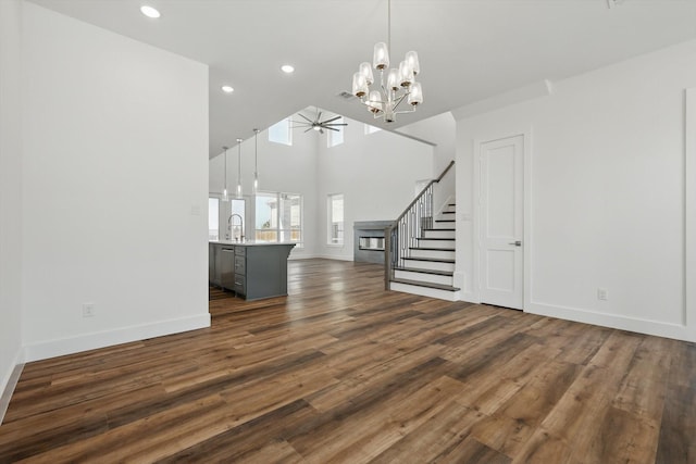 unfurnished living room with stairs, dark wood-style flooring, a sink, baseboards, and ceiling fan with notable chandelier