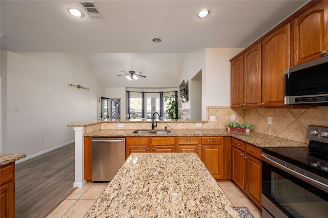 kitchen with sink, stainless steel appliances, light stone counters, decorative backsplash, and kitchen peninsula