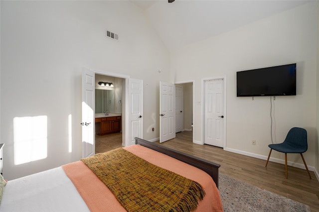 bedroom with ensuite bathroom, high vaulted ceiling, and light hardwood / wood-style floors