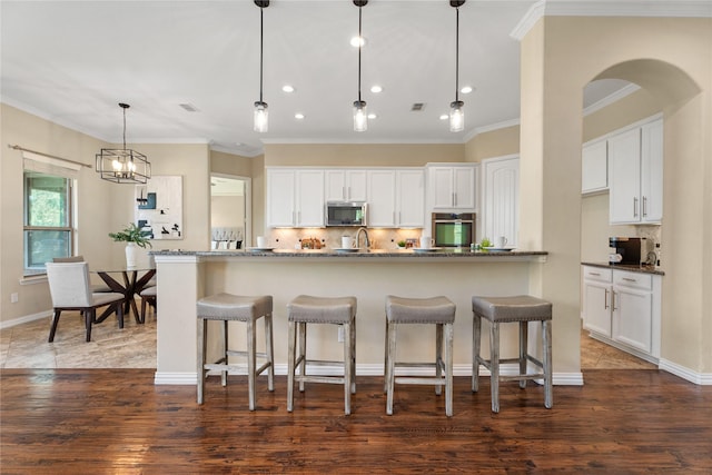 kitchen with dark stone countertops, stainless steel appliances, decorative light fixtures, and white cabinets