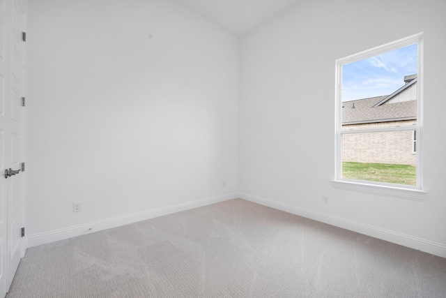 spare room featuring light carpet, lofted ceiling, and baseboards