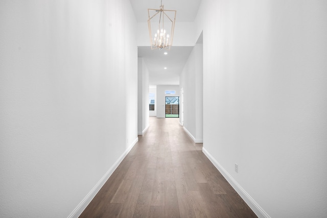 corridor with an inviting chandelier, dark wood finished floors, and baseboards