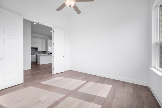 spare room with ceiling fan, light wood finished floors, and baseboards