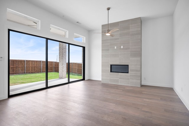 unfurnished living room with ceiling fan, a fireplace, baseboards, and wood finished floors