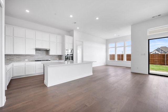 kitchen featuring under cabinet range hood, visible vents, stovetop, tasteful backsplash, and stainless steel microwave