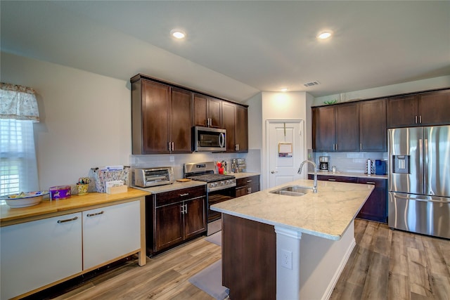 kitchen featuring stainless steel appliances, light stone countertops, sink, and dark brown cabinets