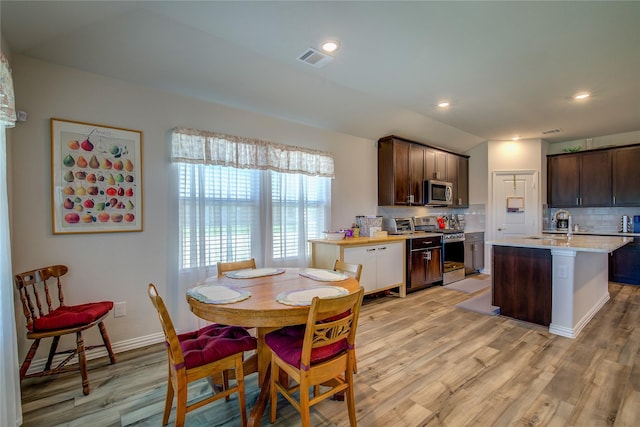 kitchen with tasteful backsplash, stainless steel appliances, dark brown cabinets, a center island with sink, and light hardwood / wood-style flooring