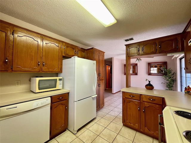 kitchen with light tile patterned flooring, white appliances, kitchen peninsula, and a textured ceiling