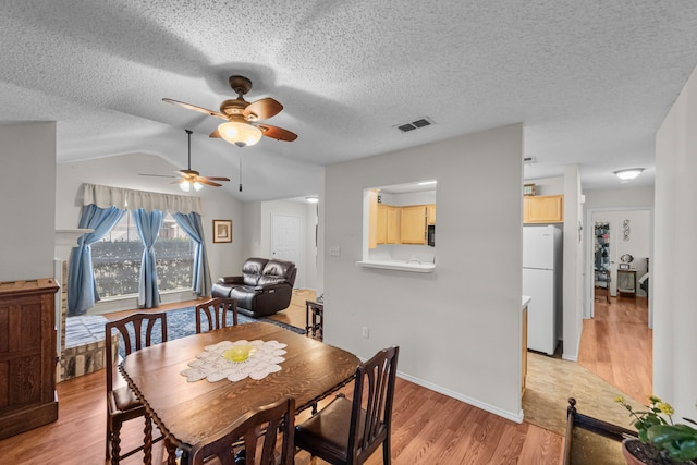 dining room featuring vaulted ceiling, a textured ceiling, and light wood-type flooring