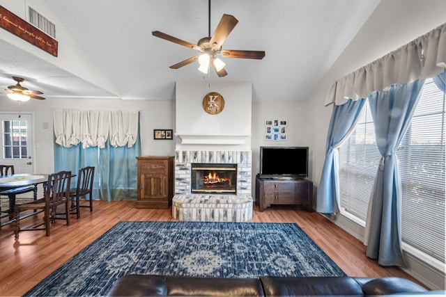 living room with wood-type flooring, lofted ceiling, ceiling fan, and a brick fireplace