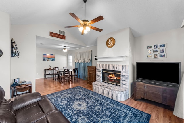 living room with wood-type flooring, vaulted ceiling, ceiling fan, and a brick fireplace